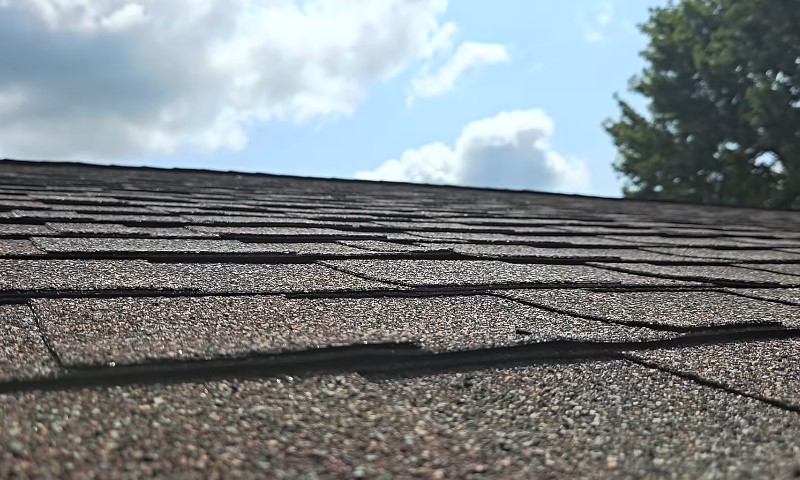 Why Roof and Gutter Maintenance Matters for Commercial Buildings 3 Close-up of a sunlit asphalt shingle roof under a partly cloudy sky