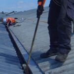 Workers in safety gear are clearing debris from a corrugated metal roof