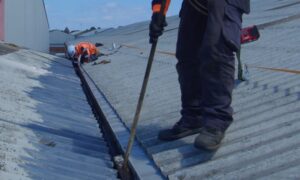 Workers in safety gear are clearing debris from a corrugated metal roof