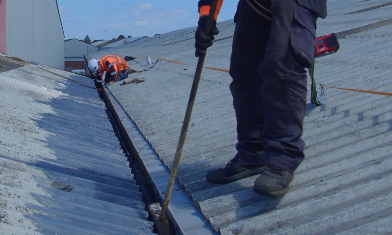Workers in safety gear are clearing debris from a corrugated metal roof
