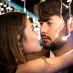Couple gazing closely at each other beneath warm string lights, capturing the feeling of instant romantic chemistry.