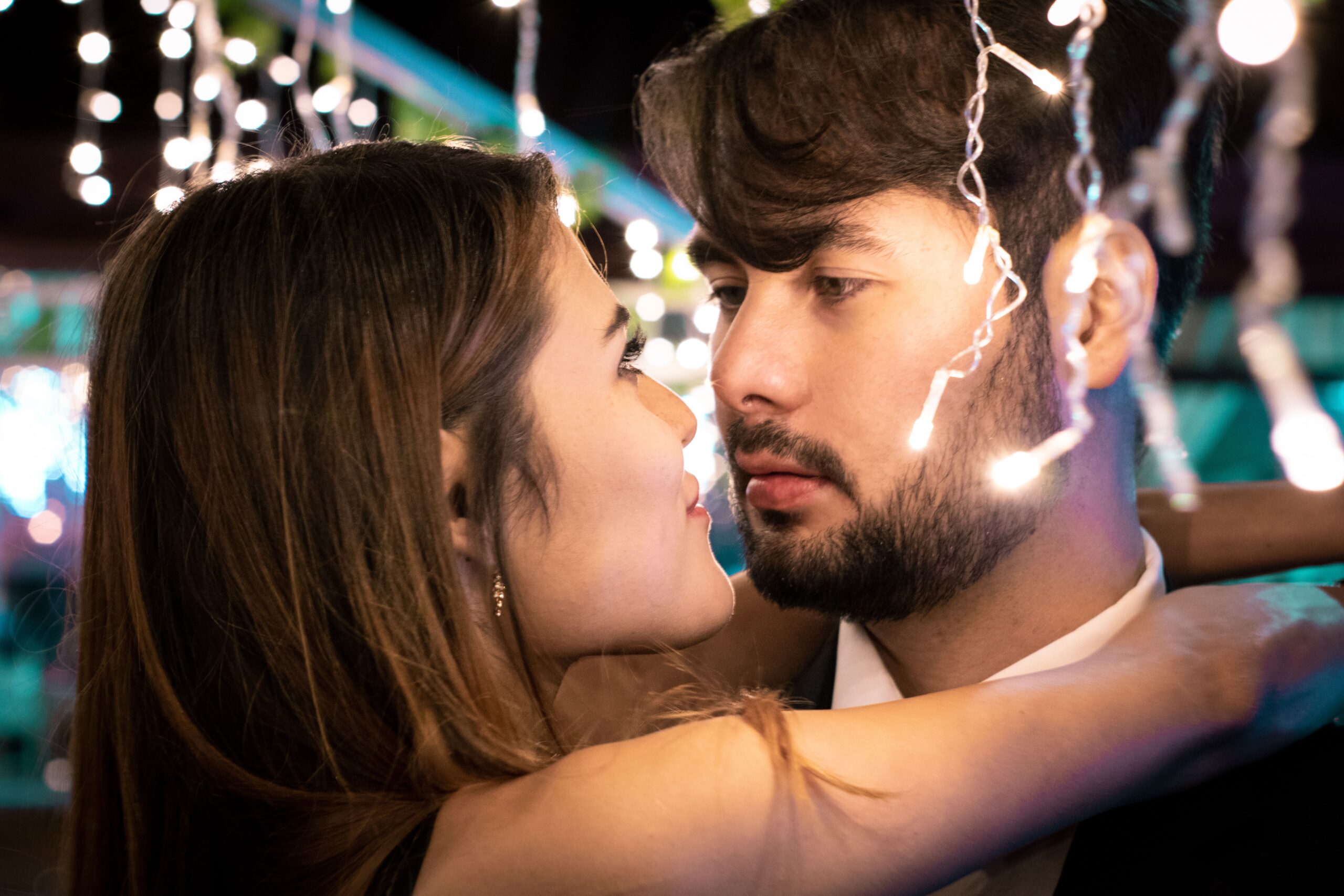 Couple gazing closely at each other beneath warm string lights, capturing the feeling of instant romantic chemistry.